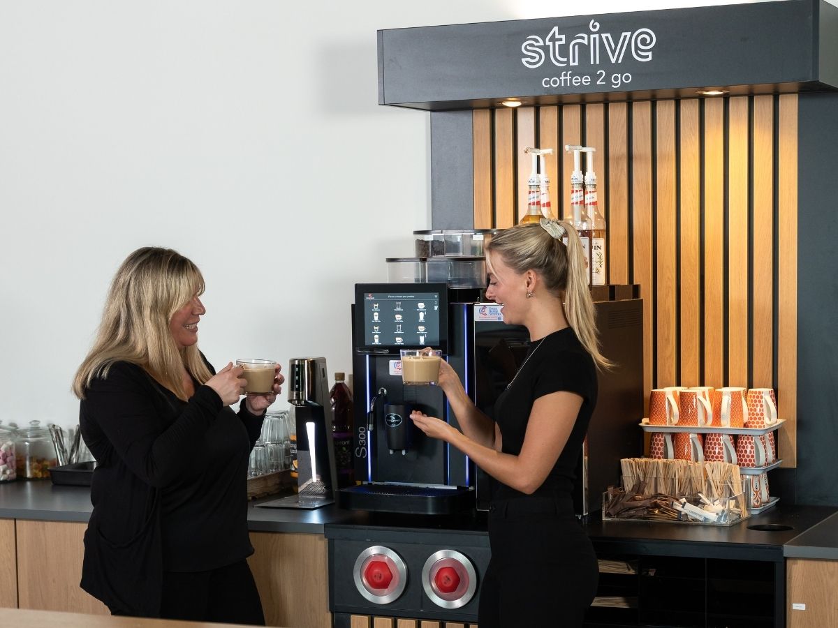 wo women smiling and drinking fresh coffee from a Strive bean-to-cup office coffee station